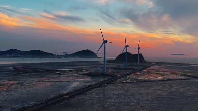 Scenic aerial view of three wind turbines standing along Tando Sea Road mudflats during a vibrant sunset with Nue Island in background Ansan South Korea