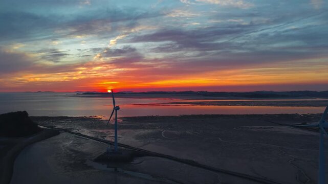 Cinematic drone shot of sunset sky reflecting on mudflats with wind turbines along Tando Sea Road path toward Nue Island in Ansan South Korea