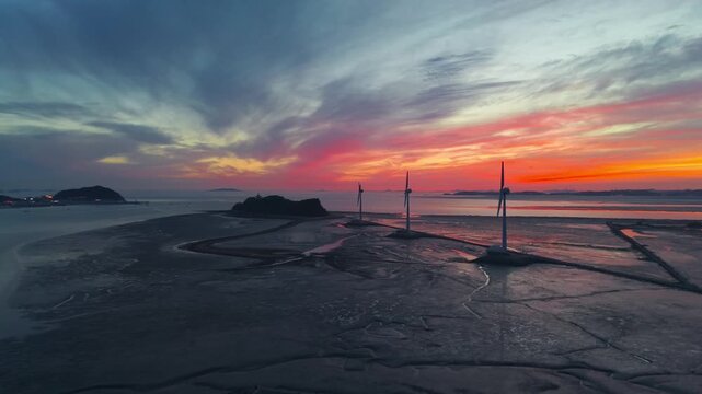 Drone shot of golden sunset sky reflecting on tidal flats at Tando Port sea road featuring three large wind turbines leading to Nue Island in Ansan South Korea