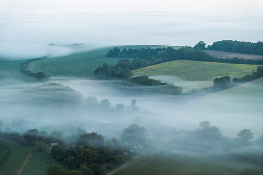 Aerial view of rolling green hills and lush fields shrouded in thick morning mist and fog Nuffield, Oxfordshire, United Kingdom.
