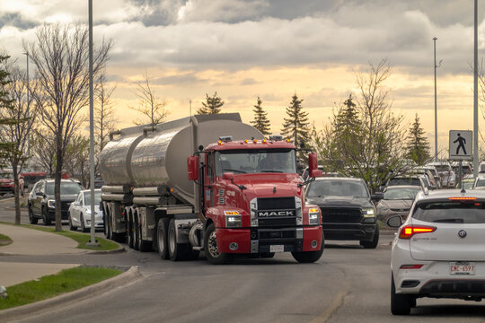 Calgary, Alberta, Canada. May 11, 2026. A red Mack tanker truck hauls a dual-trailer fuel shipment through city traffic at golden hour.