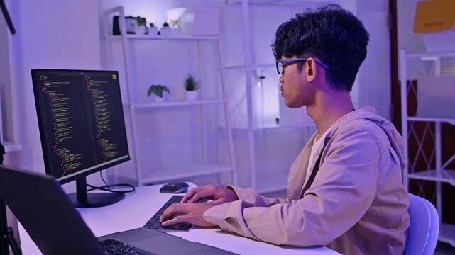 Young Asian Male Programmer Write Code On Computer Monitor In Dark Room