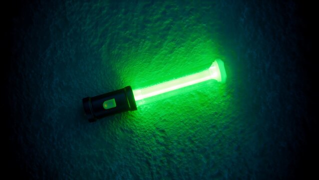 A black flashlight emits a bright, glowing green beam of light across a dark, textured surface, creating a dramatic, illuminated effect