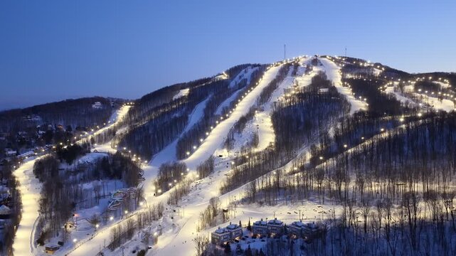 Aerial drone view of illuminated Bromont ski resort slopes at dusk, Quebec, Canada in winter. g.