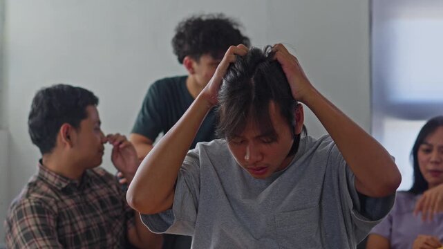 Pained expression of young man feeling judged and isolated during group gathering indoors