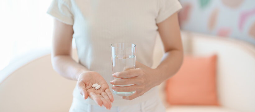 woman hand holding medicine painkiller pill and water glass on the sofa at home, taking for headaches, stomach ache, Diarrhea Pain from food poisoning, Endometriosis, Hysterectomy and Menstrual