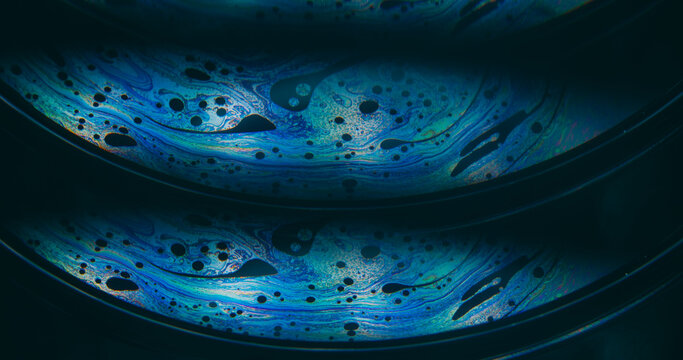 Dye water. Rainbow pollution. Blur blue purple green colorful chemical round oil water liquid leak on abstract dark black background.