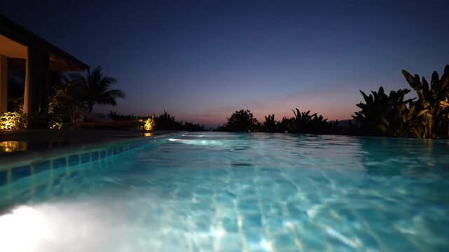 Luxury infinity pool at dusk with glowing water and tropical foliage creating serene evening atmosphere