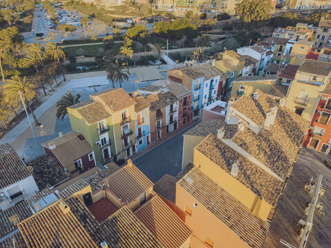Aerial view of colorful traditional houses with tiled rooftops and palm trees lining a quiet street in the historic center La Vila Joiosa, Valencian Community, Spain.