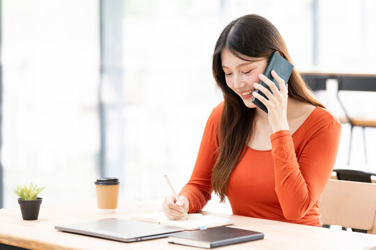 Happy Asian woman talking on phone while working in cafe