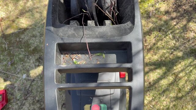 Video of a garden wood chipper in action on a sunny May day. Spring garden cleanup, pruning shrubs and trees, and recycling branches for mulch