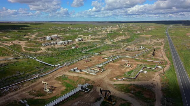 Cinematic Aerial view pipeline network converging with highway, pumpjacks lining roadside and valve stations peppering landscape, maintenance tracks and junctions visible under dynamic cloudscape,