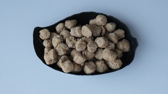 Top view of dry soya chunks in a black leaf-shaped bowl on a white background