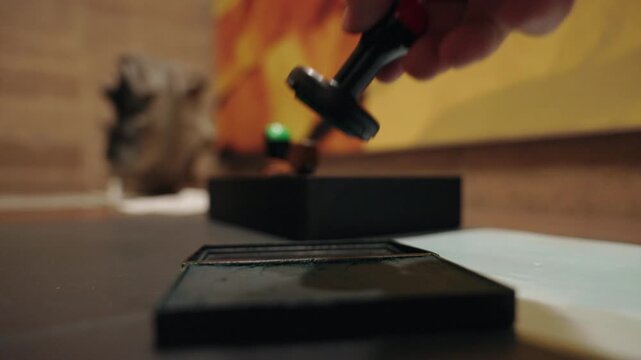 Close-up cinematic shot of hand carefully opening stamp box to reveal please close label inside warm workshop setting with soft ambient lighting and colorful orange and yellow backdrop with.