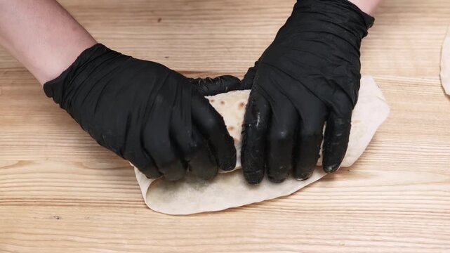 Pita sandwich. Preparing burrito. Chef cooking shawarma on kitchen table. Gloved hands wrapping flatbread with chicken vegetables sauce.