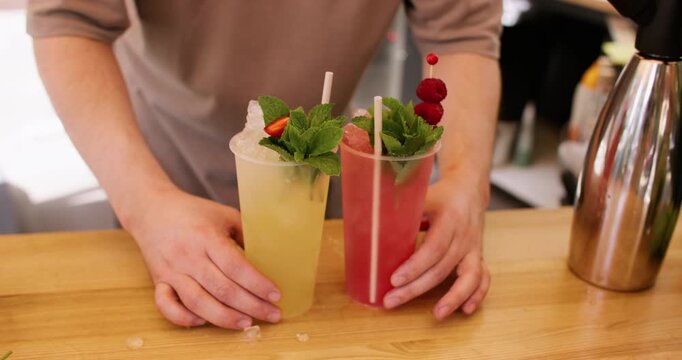 Serving cocktail. Fresh drinks. Unrecognizable barman hand adding straw mint leaves raspberries with crushed ice at professional bar counter.