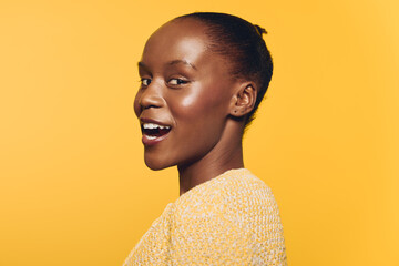 Smiling African woman with dark skin wears yellow sweater against bright yellow background. Side profile portrait with natural makeup and joyful expression. Concept of happiness and beauty. © SHOTPRIME STUDIO