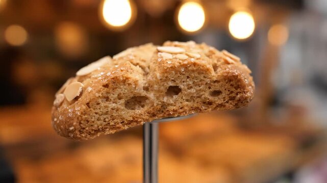 Delicious close-up of a freshly baked almond cookie sprinkled with coarse sugar crystals, displayed against a warm, blurred bakery background with bokeh lights.