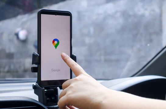 Female driver opening Google Maps on smartphone mounted inside car dashboard for GPS navigation, route directions and travel assistance while driving. Depok, Indonesia 11 May 2026.