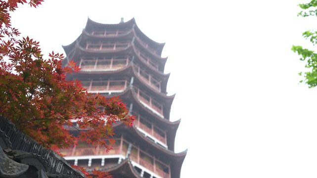 Historic wooden pagoda in Suzhou, China, framed by red maple leaves against a misty sky