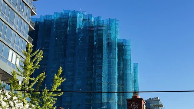 High-rise building under construction wrapped in blue mesh netting on a clear day