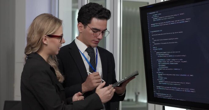 Two professionals analyze and discuss programming code displayed on screen in modern tech workspace. Capturing a collaborative environment focused on software development, debugging, and teamwork
