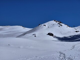 Fototapeta premium Expansive snow-covered ridge with footprints and wind patterns at Gorson Bugyal, Auli region.