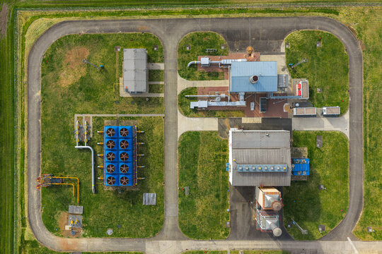 Aerial view of an industrial facility with cooling units, pipes, and buildings surrounded by green lawns and a perimeter road in Hrusky, South Moravian Region, Czechia.