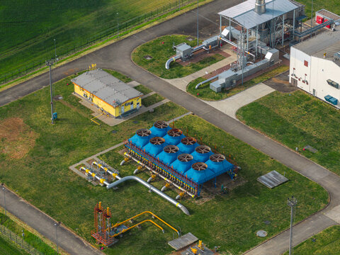 Aerial view of an industrial facility with blue cooling units, yellow pipelines, and technical buildings surrounded by green fields Hrusky, South Moravian Region, Czechia.