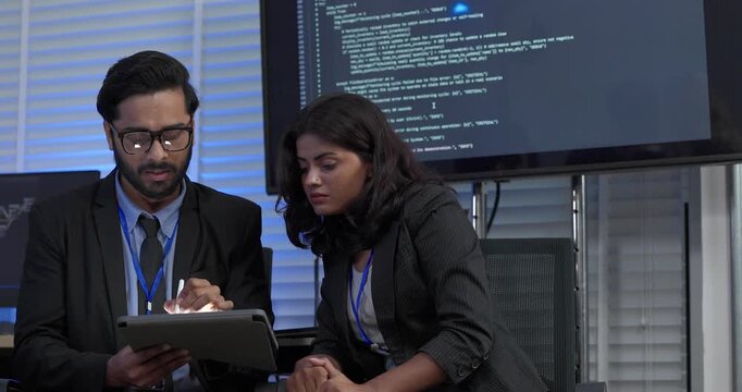 Two professionals analyze and discuss programming code displayed on screen in modern tech workspace. Capturing a collaborative environment focused on software development, debugging, and teamwork
