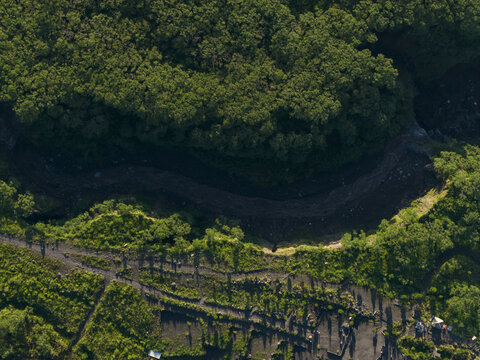 Aerial view of the Bunker Kaliadem Merapi area featuring a lush green forest canopy and dark volcanic riverbed in Kecamatan Pakem, Daerah Istimewa Yogya, Indonesia.