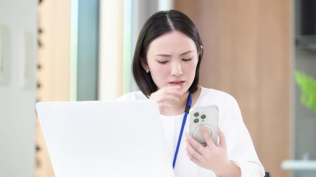 パソコンを前に忙しくて連絡が来るスマホを見たりマルチタスクで悩む考える困るオフィスカジュアルの女性、繁忙期や忙しいタスク管理ビジネスイメージ動画　