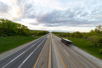 Fototapeta premium A slow shutter photo creating blur of a white semi truck with a black trailer driving down the highway road. 