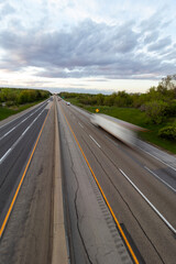 Fototapeta premium A slow shutter photo creating blur of a white semi truck with a black trailer driving down the highway road. 