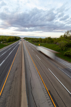 A slow shutter photo creating blur of a white semi truck with a black trailer driving down the highway road. 