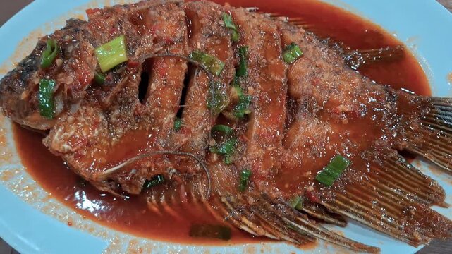 Indonesian sweet and sour gourami fish served with crispy fried gurame and rich sweet sour sauce, topped with fresh vegetables and spices. Traditional Asian seafood cuisine popular in Indonesian.