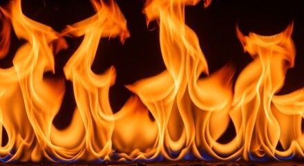 Fototapeta premium Bright orange and yellow flames burning against a dark black background, abstract fire texture.