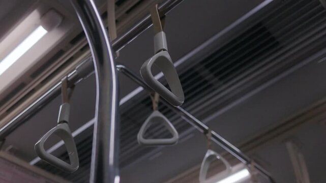 Close up shot inside a public train showing hanging hand straps swaying gently as the vehicle moves. Captures the everyday commuting atmosphere in an urban environment, with a focus on minimal design