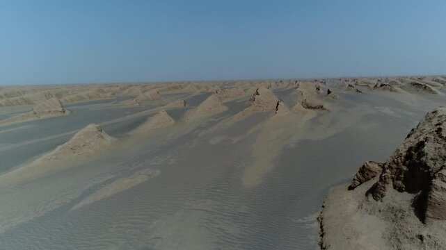 Aerial drone reveals isolated yardang rock rising from flat desert plain with sand dunes in background under bright sunlight in Iranian arid landscape stock video.