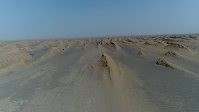 Wide aerial view captures solitary yardang rock formation standing in endless sandy desert with distant dunes and clear sky in central Iran stock video footage.