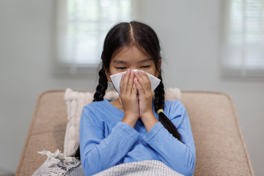 Young girl blowing nose covering face with tissue
