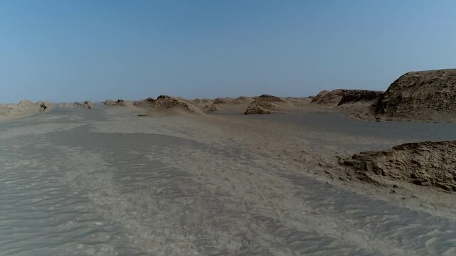 Aerial view reveals wind-eroded yardang rock standing alone in vast sandy plain with distant dunes and bright sunlight in central Iran cinematic stock footage.