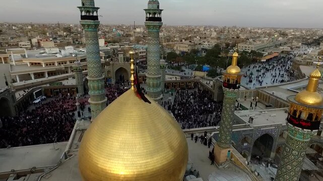 Drone circles the golden dome of Lady Masoumeh shrine at golden hour with intricate tile patterns and pilgrims moving in the large courtyard below in Qom Iran cinematic stock video.
