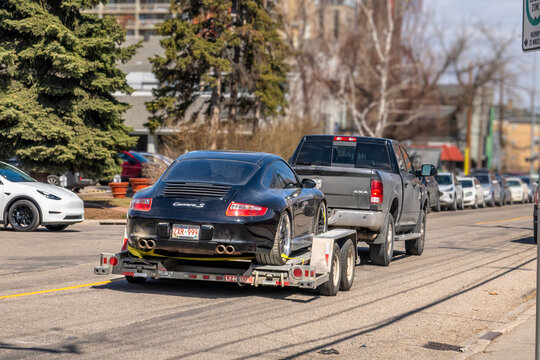 Calgary, Alberta, Canada. May 9, 2026. Rear view of a black Porsche 911 Carrera S being towed on a U-Haul trailer by a grey pickup truck.