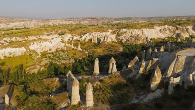 Goreme, Nevsehir, Turkey. Aerial sweep across Love Valley's towering fairy chimneys, their basalt-capped tuff pillars glowing in warm evening light.. Aerial View, MasterShots, Spiral forward