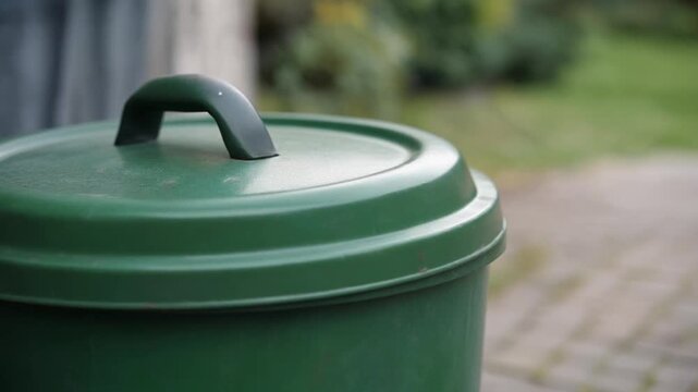Green compost bin with lid open outdoors.