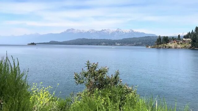 Breathtaking panoramic landscape of crystal-clear Nahuel Huapi Lake surrounded by dense Andean forests and snow-capped mountains. Sunny day with blue sky, located in Nahuel Huapi National Park, Neuque
