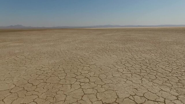 Vast cracked salt flat stretches endlessly toward hazy horizon with geometric mud polygons baking under intense midday sun in arid Iranian desert cinematic aerial stock footage.