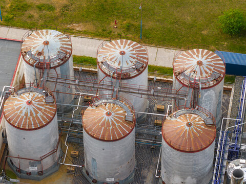 Aerial view of six large industrial storage tanks with rusty conical roofs and connecting metal walkways in Breclav, South Moravian Region, Czechia.
