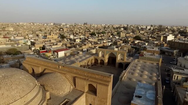 Aerial drone captures golden dome shrine rising above dense rooftops in historic Qom old city Iran with traditional mudbrick architecture narrow winding alleys and clear blue sky cinematic stock